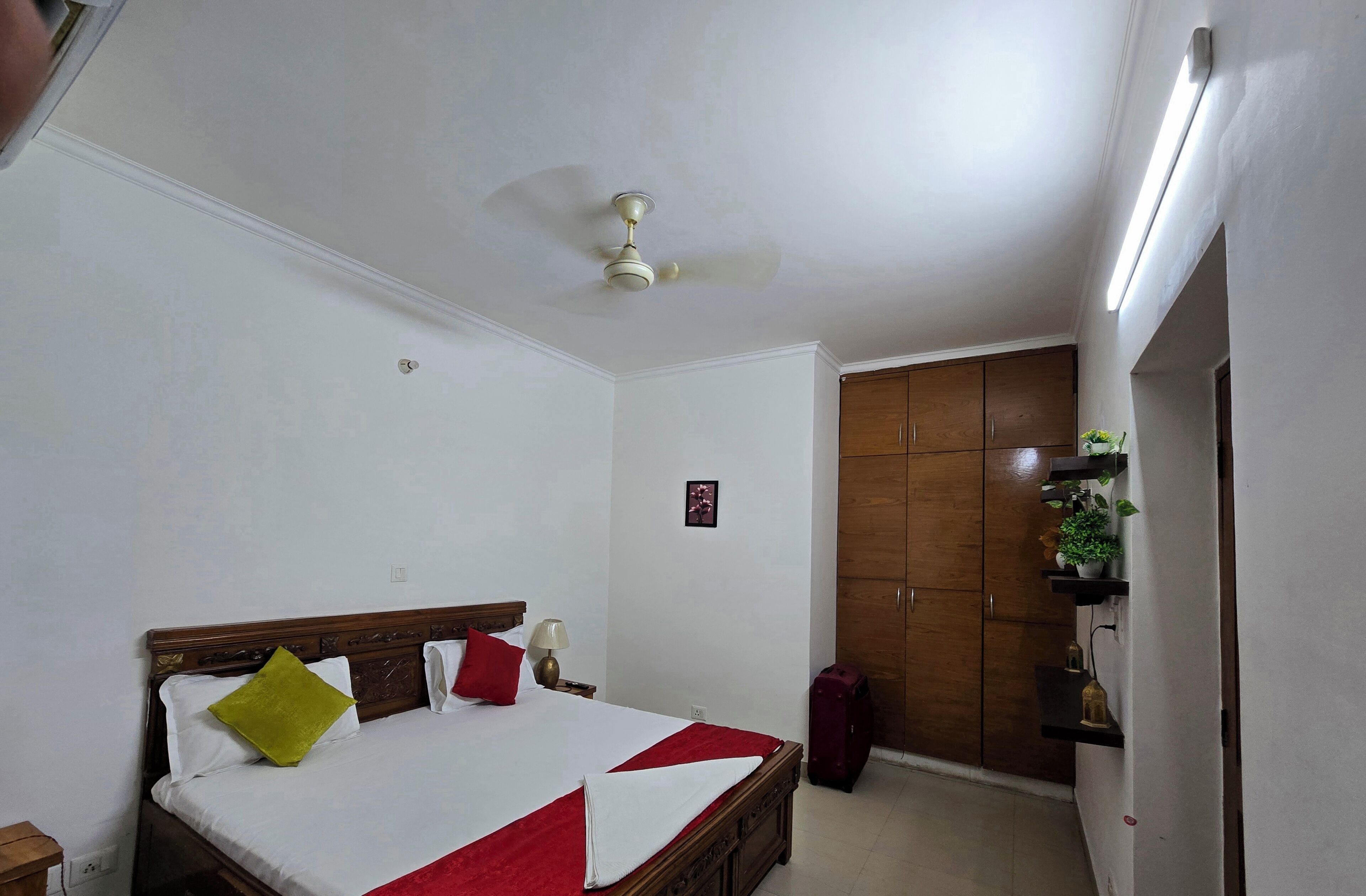 Une chambre d’hôtel avec un lit, un ventilateur de plafond, une armoire et une petite plante posée sur une étagère.