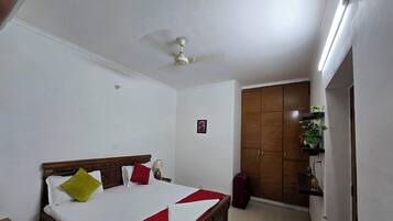 A hotel room with a bed, a ceiling fan, a wardrobe, and a small plant on a shelf.