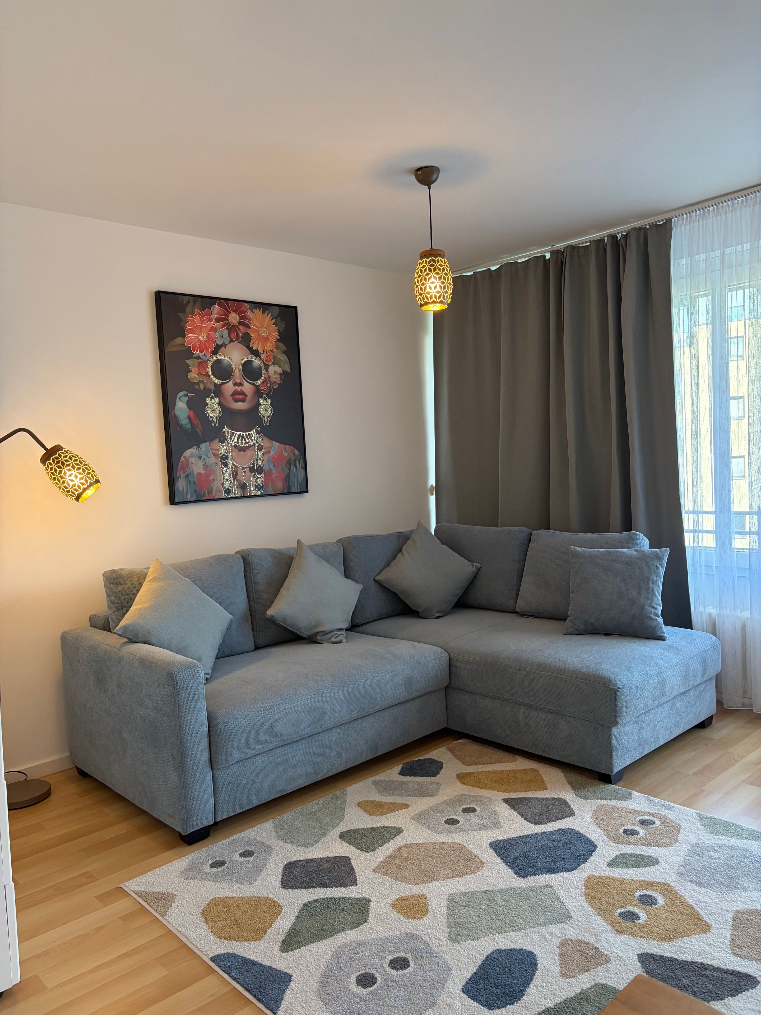 A modern living room with a grey sectional sofa, a patterned rug, and a wall-mounted artwork.