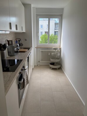 Una cucina moderna con mobili bianchi, forno integrato, microonde e una finestra con vista sugli edifici.