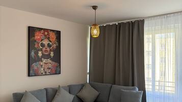 Een moderne woonkamer met een grijze hoekbank, een kamerkleed met dessin, een hanglamp en een schilderij aan de muur.