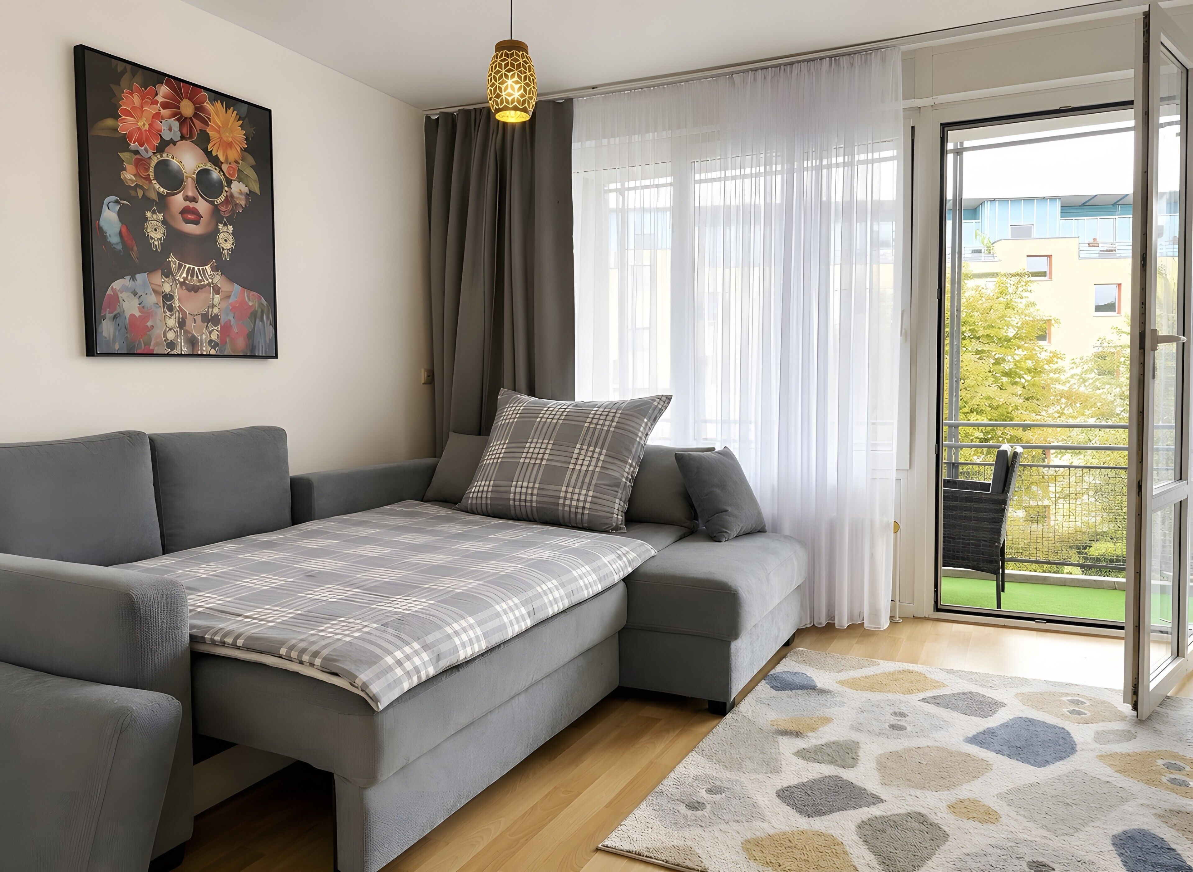 Una sala de estar moderna con un sofá gris, un plaid estampado y vistas al exterior a través de grandes ventanales.