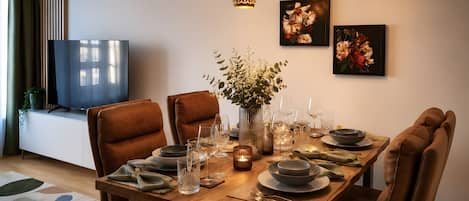 A dining area with a wooden table set for four, surrounded by leather chairs, with a vase of flowers and candle holders on the table.
