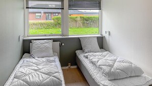 Um quarto pequeno com duas camas de solteiro, um radiador e uma janela com persianas.