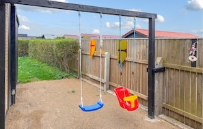 A wooden swing set with two swings, a fence, and a small garden area. - Awesome home in Thyborøn with WiFi (Thyborøn)