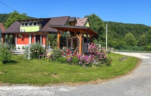A two-story house with a porch, surrounded by a well-maintained garden with various flowers and shrubs. - Awesome apartment in Hreljin Ogulinski with sauna (Hreljin Ogulinski)