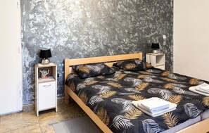 A bedroom with a bed, two bedside tables, a nightstand, a lamp, and a wall with a textured pattern. - Awesome apartment in Hreljin Ogulinski with sauna (Hreljin Ogulinski)