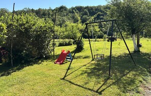 A playground with a swing set and a slide in a grassy area with trees. - Awesome apartment in Hreljin Ogulinski with sauna (Hreljin Ogulinski)