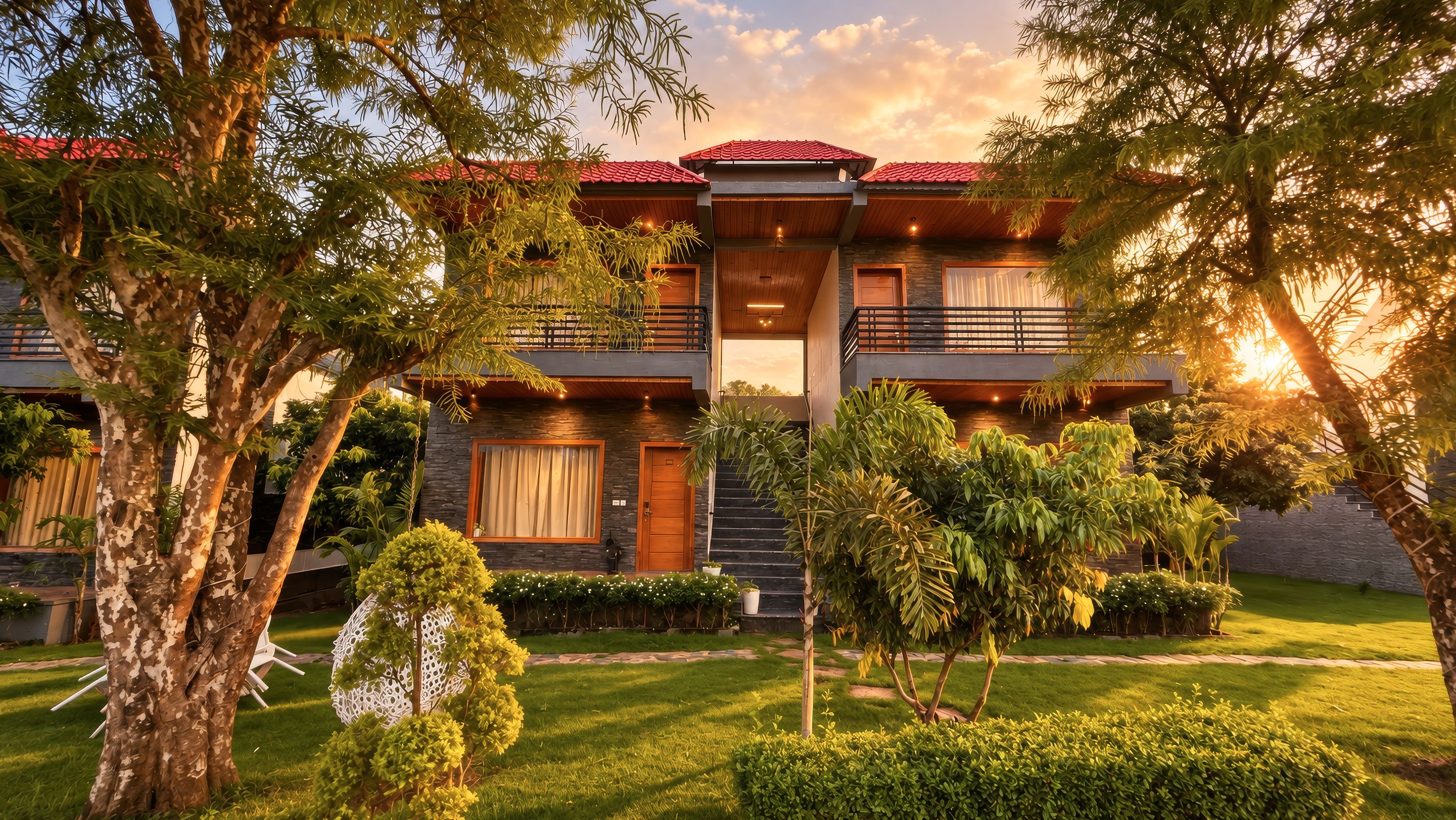 A two-story building with a red-tiled roof, a balcony, and a well-maintained garden with various plants and a lawn.