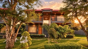 A two-story building with a red-tiled roof, a balcony, and a well-maintained garden with various plants and a lawn.