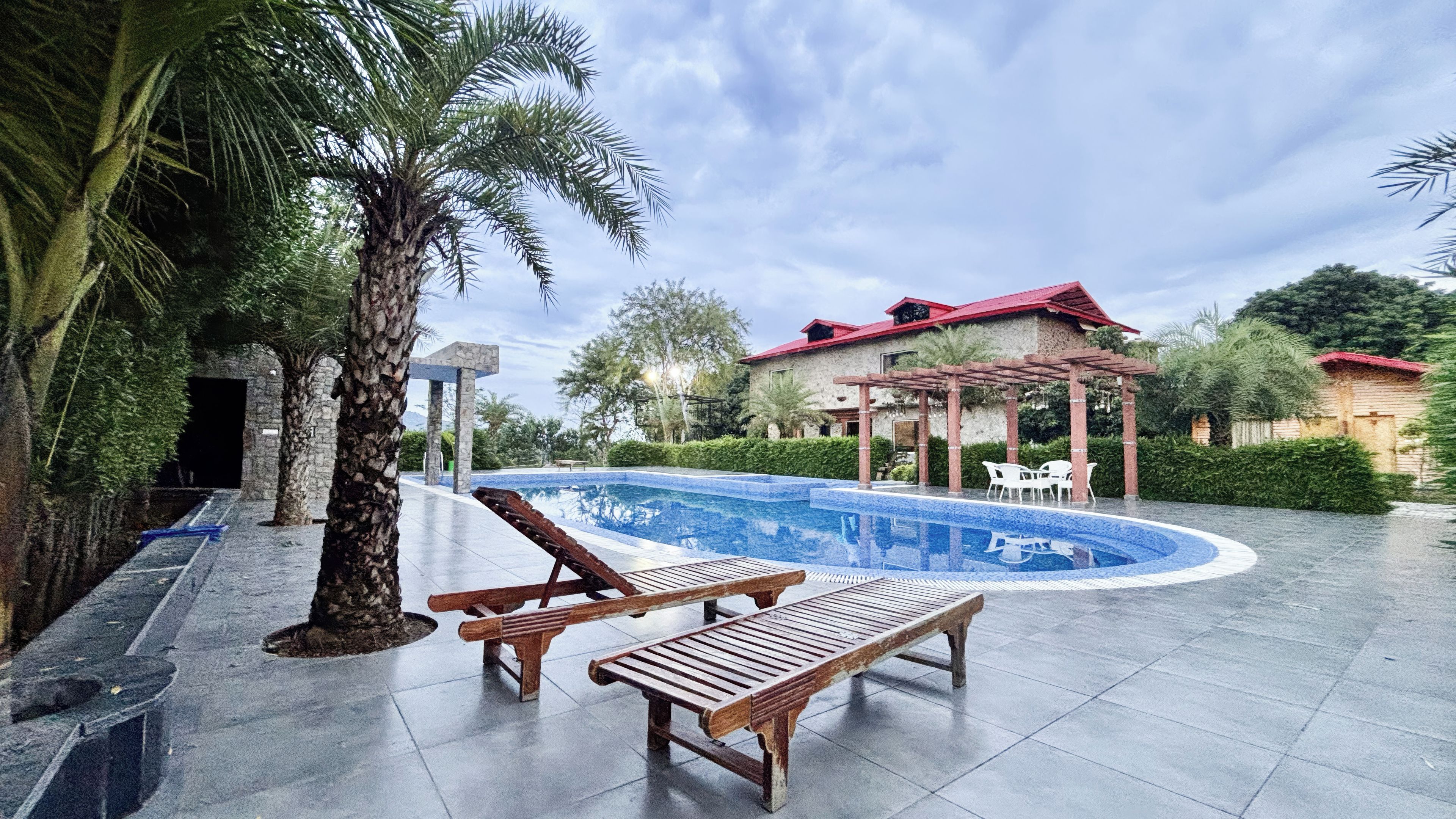 A swimming pool with lounge chairs, a stone pathway, and a building with a red roof.