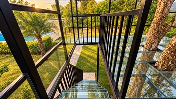 A glass-walled staircase leading to a rooftop terrace with a view of a pool and surrounding greenery.
