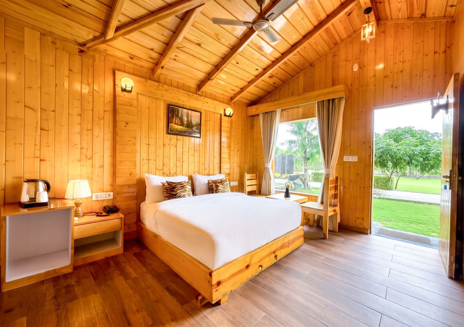 A wooden cabin room with a bed, bedside table, lamp, and a view of the outdoors.