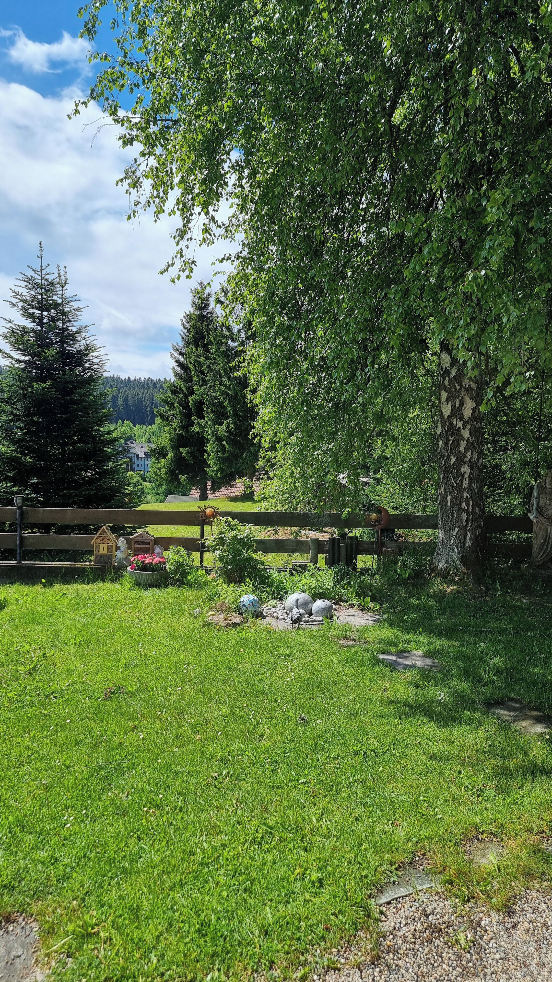 A grassy area with a wooden fence, a large tree, and a distant view of houses.