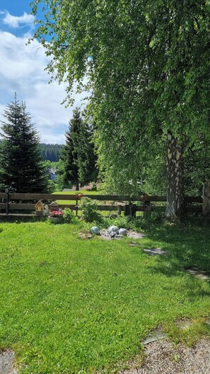 Eine Rasenfläche mit Holzzaun, einem großen Baum und einem entfernten Blick auf Häuser.