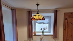 En matplats med ett bord, stolar, en hängande lampa, ett fönster med gardiner och en trädörr.