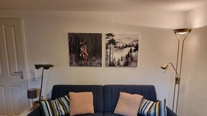 En mörkblå soffa med randiga kuddar, två tavlor som hänger på väggen, en golvlampa och en dörr.