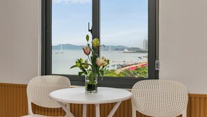 Una habitación con un ventanal grande, dos sillas blancas, una mesita redonda y un jarrón con flores.