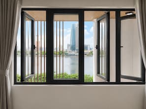 A room with a large window overlooking a cityscape and a body of water. - Ngoc Thuong Hotel & Apartment (Da Nang)