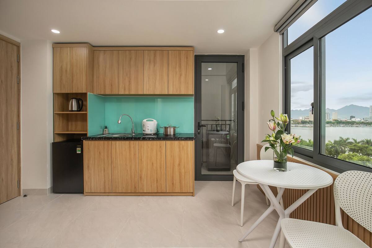 Een moderne keuken met houten kasten, een zwarte koelkast en een raam met uitzicht op een stadsbeeld.