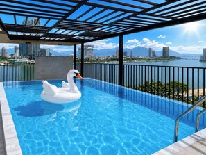 A rooftop swimming pool with a swan float, city skyline views, and a clear sky. - Ngoc Thuong Hotel & Apartment (Da Nang)