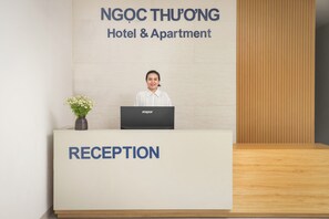 Bancada de recepção no Hotel & Apartamento NGOC THU'ONG, com um laptop, um vaso de flores e um painel de parede de madeira.