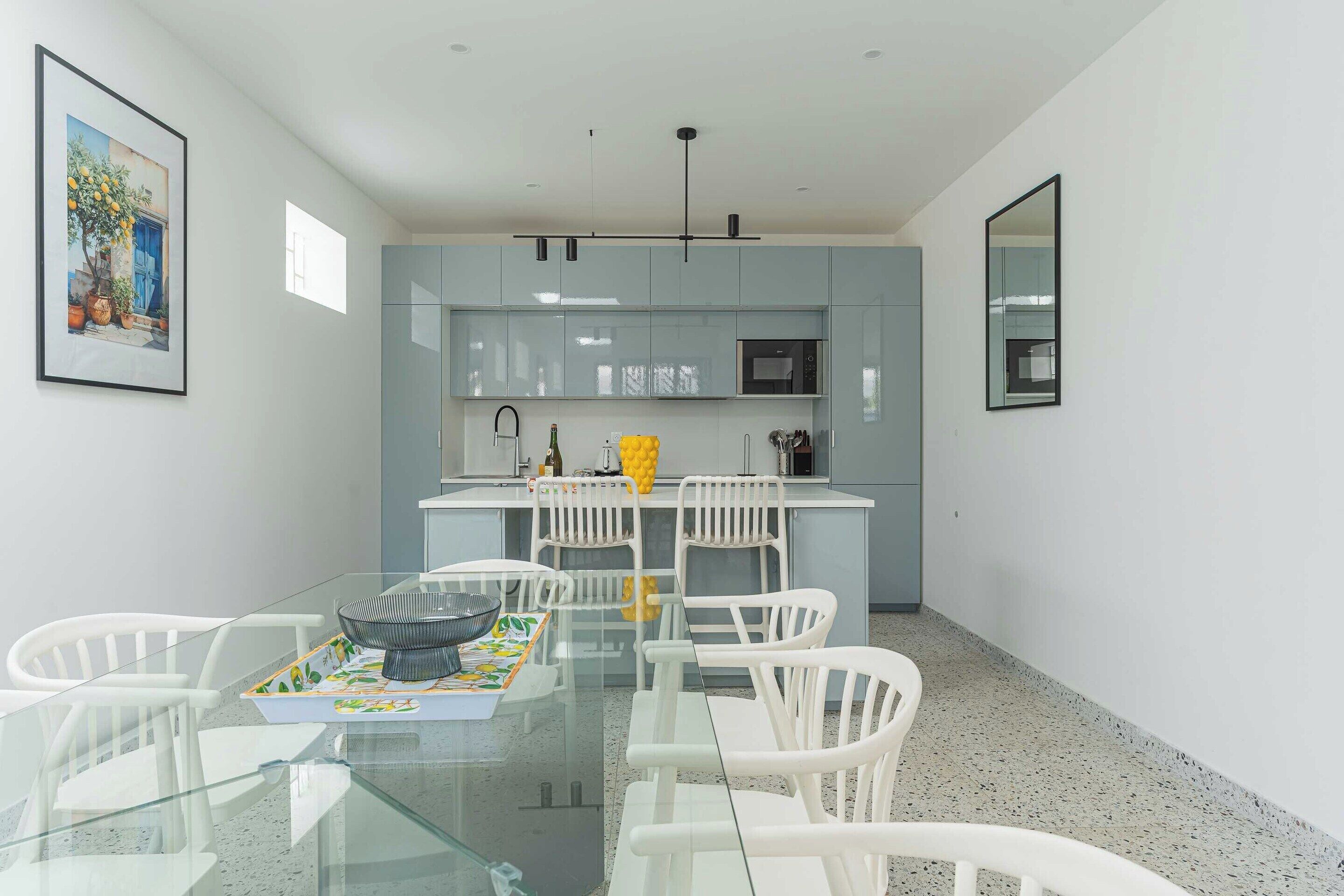 A modern kitchen with white cabinets, a central island with seating, and a dining table with chairs.