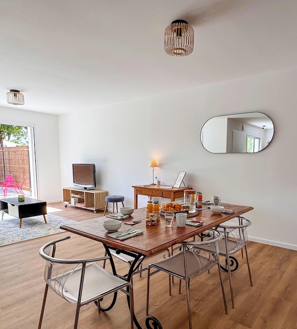 Un comedor con una mesa de madera, sillas de metal, un televisor y un espejo en la pared.