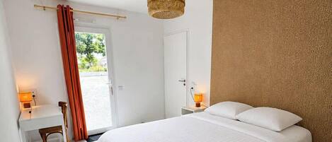 Un dormitorio con cama, mesitas de noche, escritorio, silla, lámpara colgante y puerta que da a un área exterior.