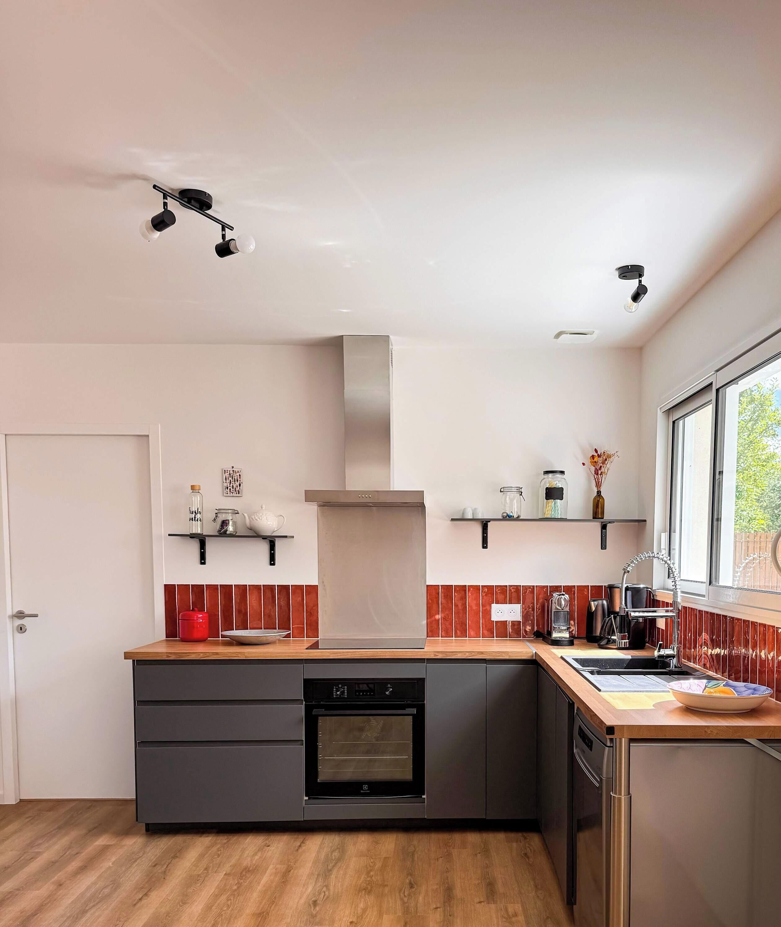 A modern kitchen with a built-in oven, a dishwasher, and a window providing natural light.