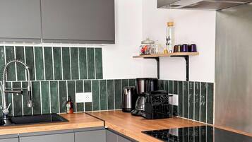 A modern kitchen with a black stove, a coffee maker, and a shelf with kitchen items.