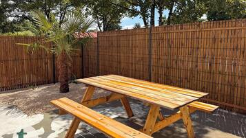 A wooden picnic table with benches in a backyard with a wooden fence and trees.