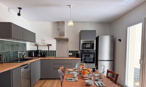 A modern kitchen with grey cabinets, a wooden countertop, and a dining table set for breakfast. - Tranquiloue - Maison Neuve - 18 min du Puy du Fou (Les Herbiers)