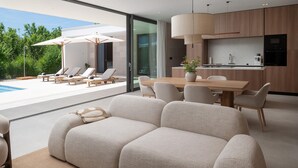 Ein moderner Wohnbereich mit Essplatz, Küche und Poollounge mit Sonnenschirmen.