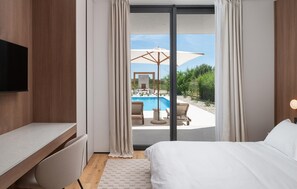 A hotel room with a bed, a TV, a desk, and a view of an outdoor pool area. - Gorgeous home in Privlaka (Privlaka)
