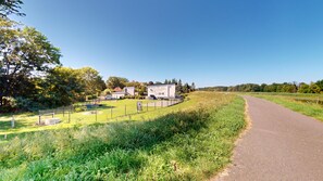 Paisagem rural com um caminho pavimentado, área cercada com um edifício e vegetação.