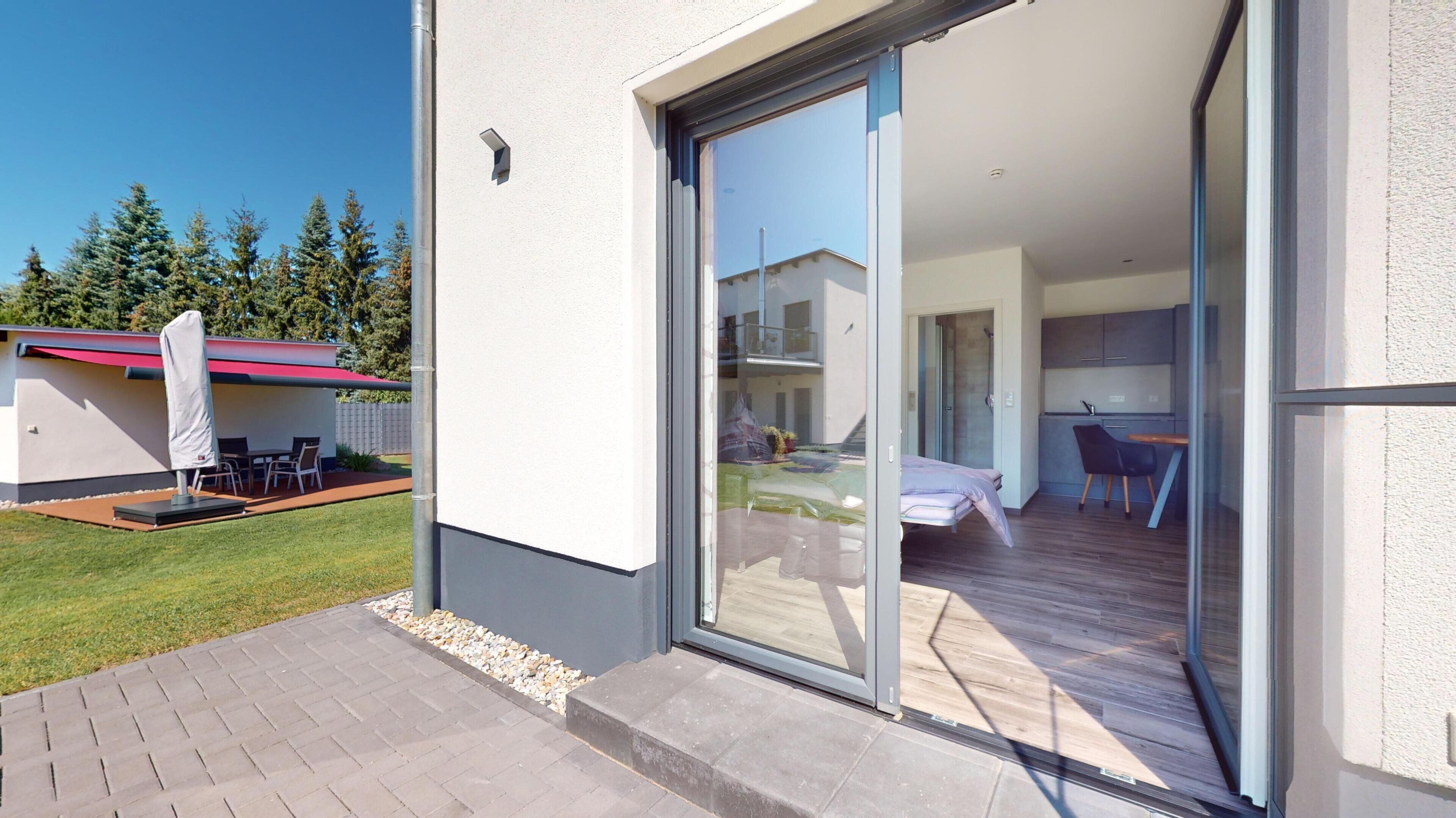 Eine moderne Wohnung mit einer Schiebetür zum Balkon, einer kleinen Sitzgelegenheit im Freien und einer sichtbaren Küche.