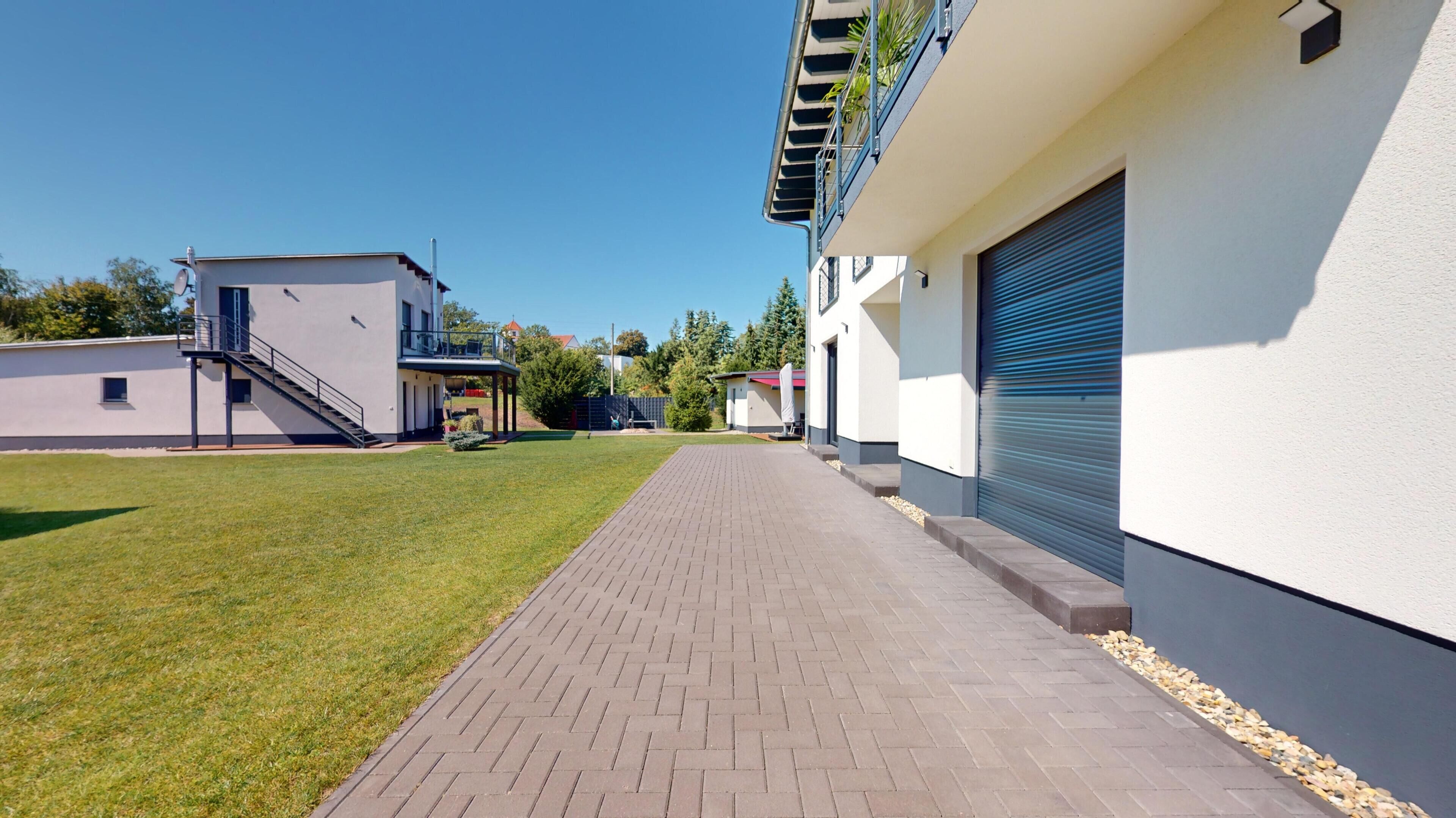 Ein modernes Gebäude mit gepflastertem Weg, einer Treppe und einer Garagentür.