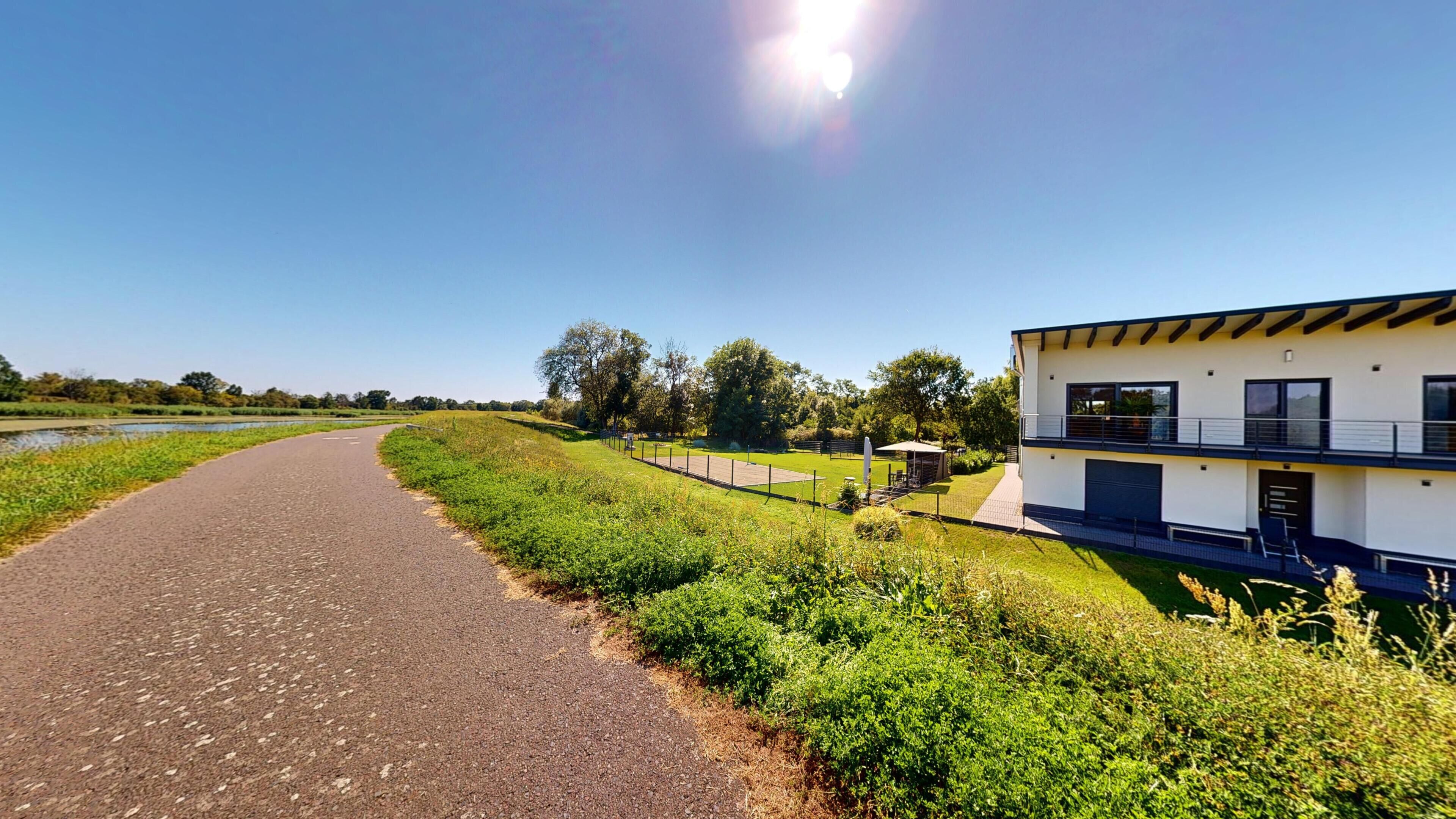 Een modern gebouw met twee verdiepingen, een plat dak, een verhard pad en een gazon met een klein vijvertje.