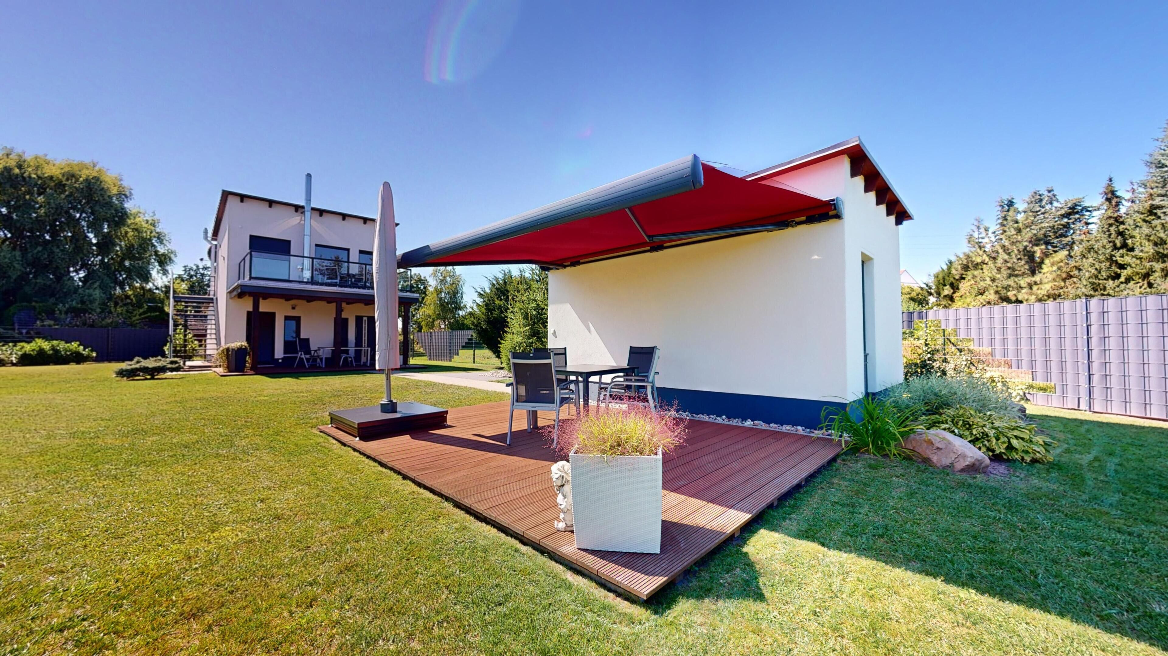 Une maison moderne dotée d’un patio, de mobilier d’extérieur et d’un auvent rouge.