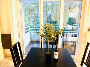 A table with a potted plant and a bottle of wine, a chair, and a view of a balcony with a railing. - Quiet 3-room apartment in Gradignan, near Bordeaux (Gradignan)