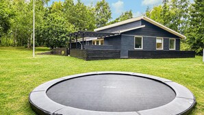 En bostadsfastighet med en studsmatta på gården, en täckt uteplats och ett hus med en mörk fasad.