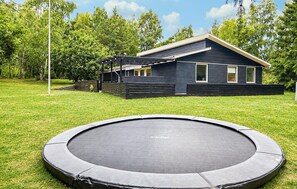 Ein Wohnhaus mit Trampolin im Garten, einer überdachten Sitzgelegenheit im Freien und einer Fassade in dunkler Farbe.
