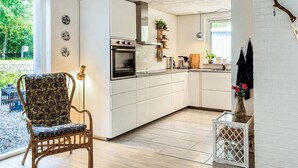 Ett kompakt kök med vita skåp, en inbyggd ugn och en matplats med en mönstrad stol.