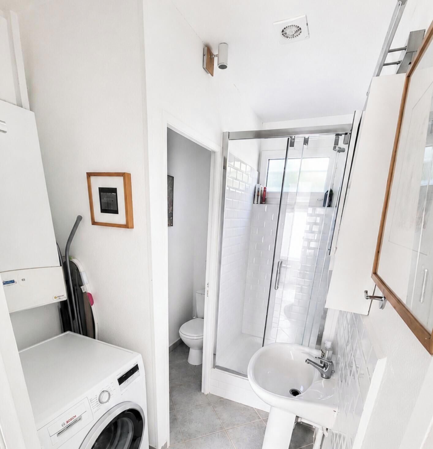 A compact bathroom with a washing machine, a sink, and a glass shower enclosure.