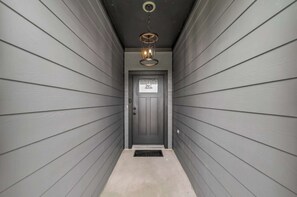 Ein schmaler Flur mit grauen Wänden und einer Tür mit Fenster, darüber eine Pendelleuchte.