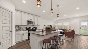 A spacious kitchen with white cabinets, a large island with stools, a microwave, and a sink. - Texas Crew Retreat:4BR, Huge Parking & TVs (Cove)