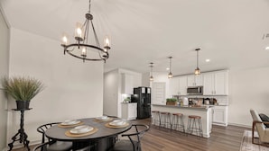 A modern kitchen with white cabinets, a central island, bar stools, and pendant lighting. - Texas Crew Retreat:4BR, Huge Parking & TVs (Cove)