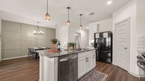 A modern kitchen with a central island, stainless steel appliances, pendant lighting, and a dining area with a round table. - Texas Crew Retreat:4BR, Huge Parking & TVs (Cove)