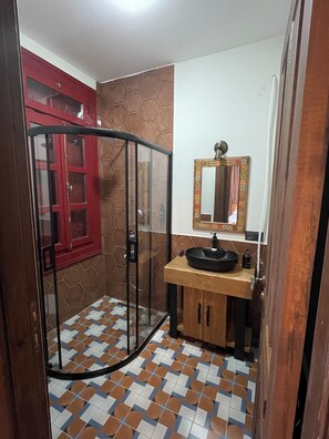 A bathroom with a glass shower enclosure, a wooden vanity with a sink, a red cabinet, and a mirror with a decorative frame. - Konak 1882 (Ayvalik)